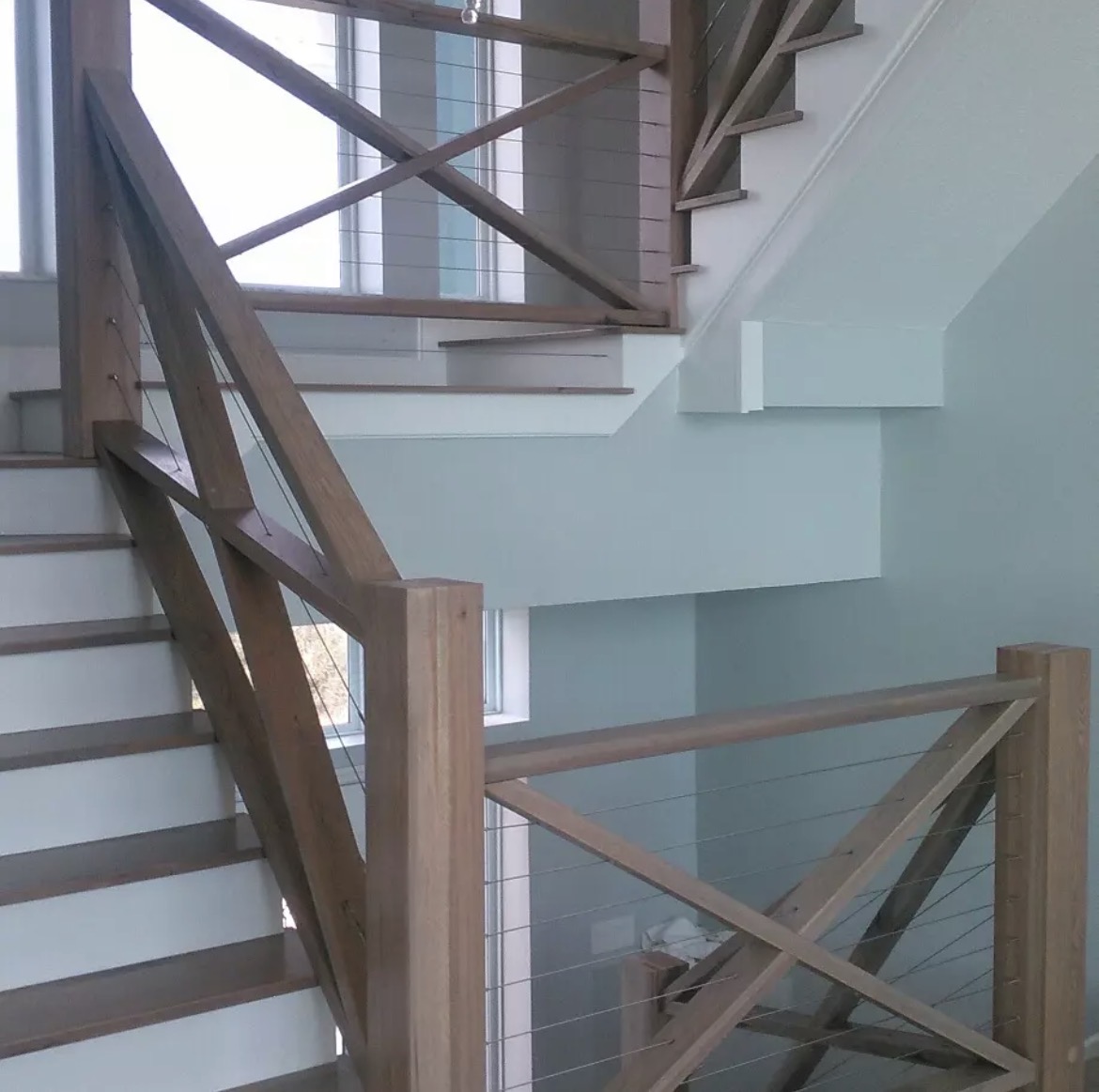 Wood staircase with cross-braced railings, horizontal cables and white risers